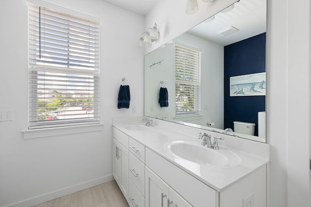 bathroom with double vanity, baseboards, and toilet
