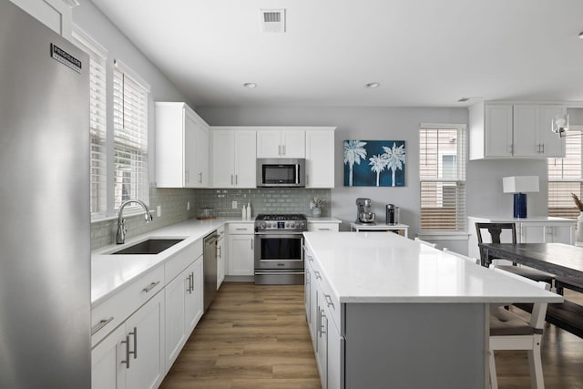 kitchen featuring stainless steel appliances, a sink, a kitchen island, wood finished floors, and tasteful backsplash