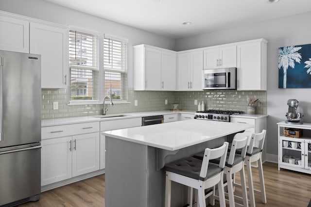 kitchen featuring stainless steel appliances, a sink, wood finished floors, a kitchen bar, and recessed lighting