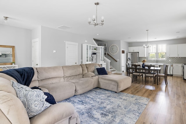 living area with a chandelier, light wood-style floors, and stairs