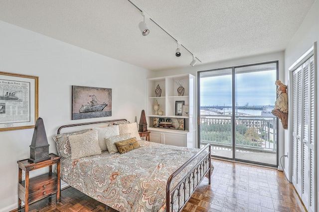 bedroom featuring a textured ceiling, access to exterior, parquet floors, and rail lighting