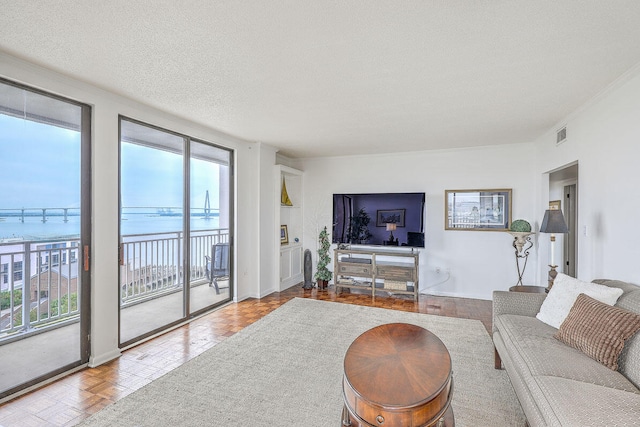 living room featuring a water view, a textured ceiling, plenty of natural light, and light parquet flooring