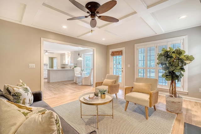 living area featuring coffered ceiling, baseboards, light wood-type flooring, and a ceiling fan
