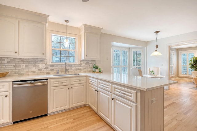 kitchen with light countertops, a sink, a peninsula, stainless steel dishwasher, and light wood-type flooring