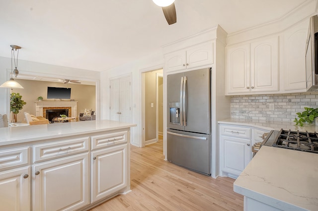 kitchen with tasteful backsplash, a brick fireplace, stainless steel appliances, light wood-style floors, and ceiling fan
