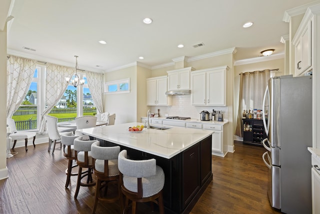 kitchen with hanging light fixtures, white cabinets, stainless steel refrigerator, and a center island with sink