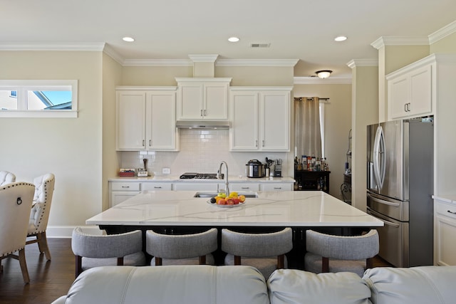 kitchen featuring appliances with stainless steel finishes, a kitchen island with sink, white cabinets, light stone counters, and sink