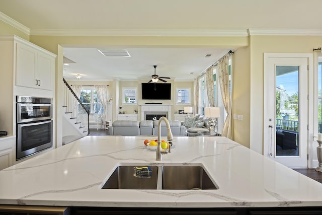 kitchen featuring sink, an island with sink, light stone counters, and ornamental molding