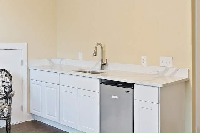 kitchen with sink, dark wood-type flooring, white cabinets, light stone counters, and dishwashing machine