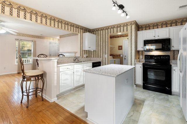 kitchen featuring separate washer and dryer, a kitchen island, white cabinetry, and black appliances