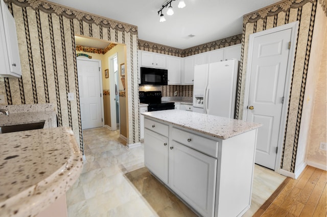 kitchen featuring white cabinets, light wood-type flooring, black appliances, a center island, and sink