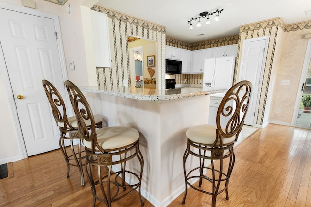 kitchen featuring white cabinets, kitchen peninsula, black appliances, a kitchen breakfast bar, and light hardwood / wood-style floors