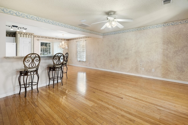 spare room featuring ceiling fan with notable chandelier, a textured ceiling, light hardwood / wood-style flooring, and track lighting