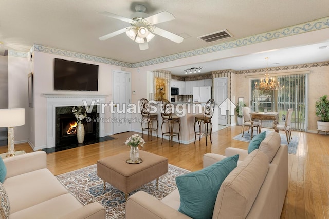 living room featuring ceiling fan with notable chandelier, light hardwood / wood-style floors, and a fireplace