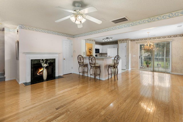 unfurnished living room with light hardwood / wood-style flooring, ceiling fan with notable chandelier, and a fireplace