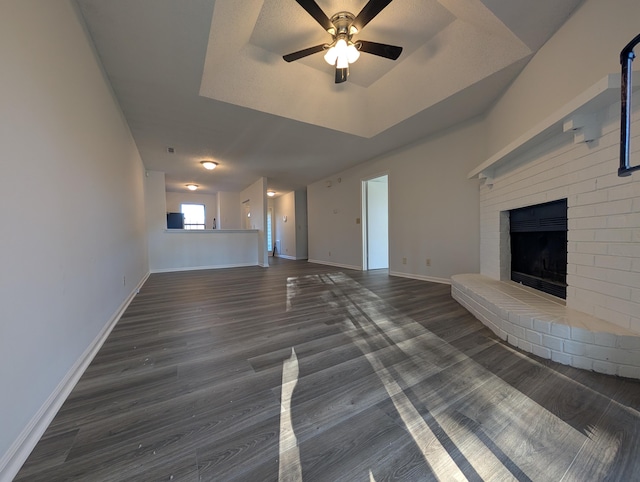 unfurnished living room featuring a tray ceiling, ceiling fan, a fireplace, and dark wood-type flooring