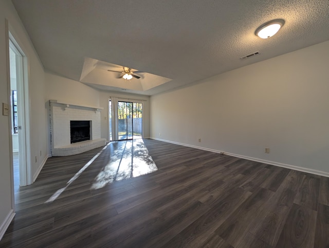 unfurnished living room featuring a textured ceiling, ceiling fan, dark hardwood / wood-style floors, and a brick fireplace