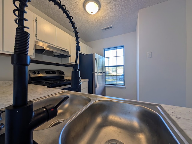 kitchen with appliances with stainless steel finishes, a textured ceiling, and white cabinetry