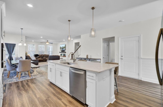 kitchen featuring a kitchen island with sink, a sink, stainless steel dishwasher, wood finished floors, and white cabinetry