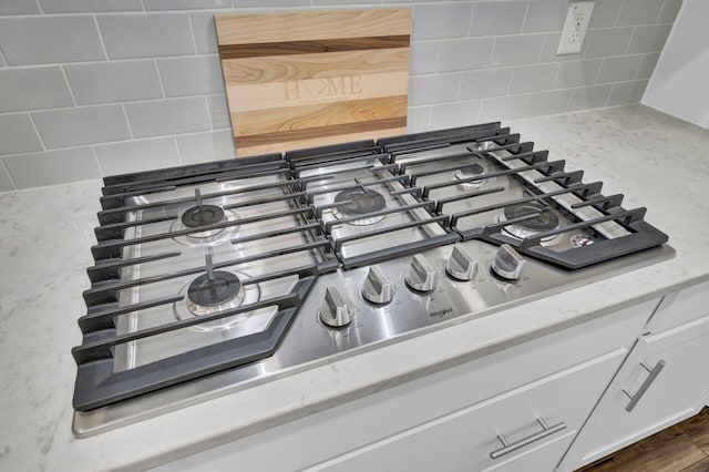 room details with decorative backsplash, stainless steel gas stovetop, and white cabinetry