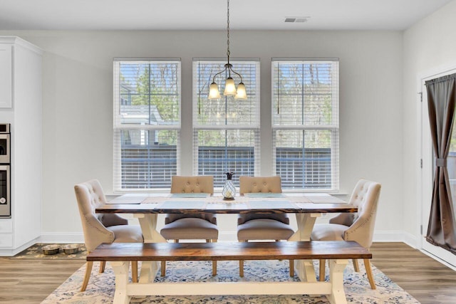 dining room featuring visible vents, light wood-style floors, a healthy amount of sunlight, and an inviting chandelier