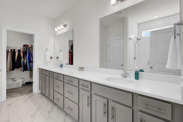 bathroom featuring a sink, tiled shower, marble finish floor, and double vanity