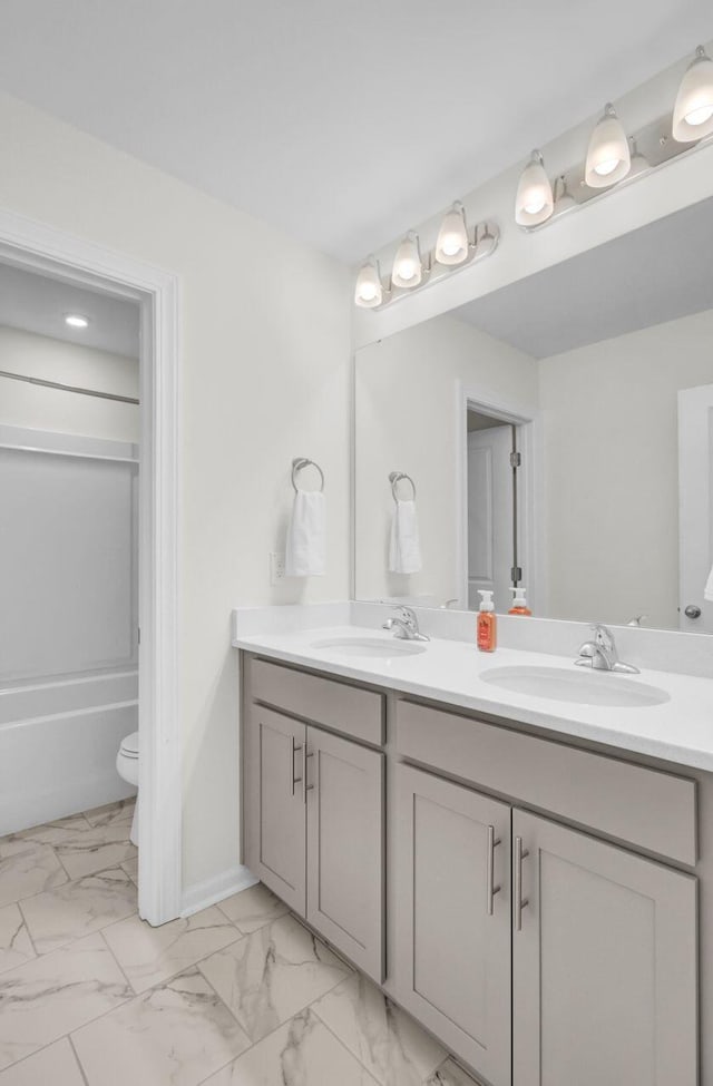 bathroom featuring double vanity, marble finish floor, toilet, and a sink