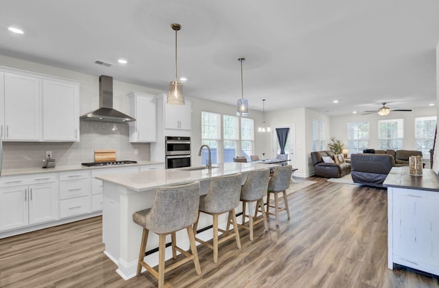 kitchen featuring a sink, stainless steel appliances, a breakfast bar area, white cabinets, and wall chimney range hood