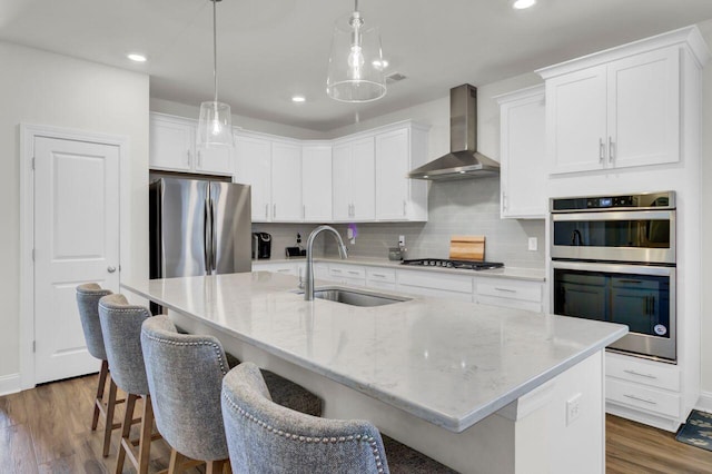 kitchen with a sink, wood finished floors, appliances with stainless steel finishes, and wall chimney exhaust hood