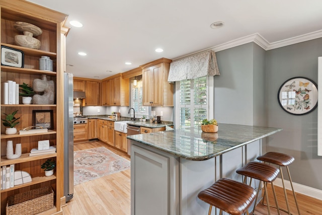 kitchen with crown molding, a kitchen breakfast bar, light wood-type flooring, under cabinet range hood, and dark stone countertops