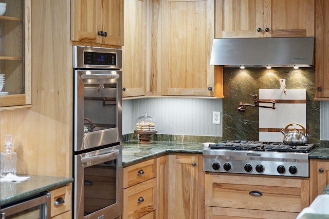 kitchen with appliances with stainless steel finishes, tasteful backsplash, range hood, dark stone countertops, and beverage cooler