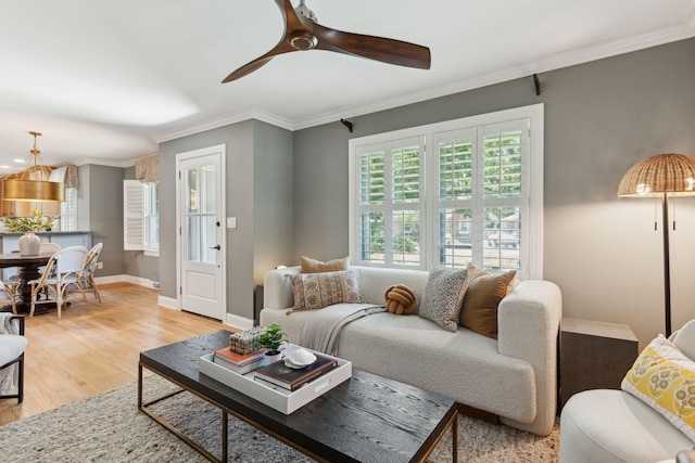 living room featuring crown molding, ceiling fan, baseboards, and light wood-style floors