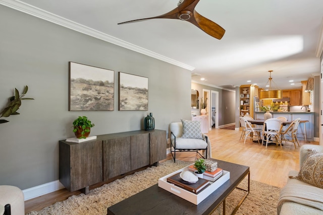 living room with a ceiling fan, baseboards, ornamental molding, and light wood-style flooring
