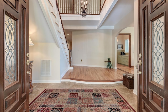 foyer entrance with arched walkways, a high ceiling, visible vents, baseboards, and stairs