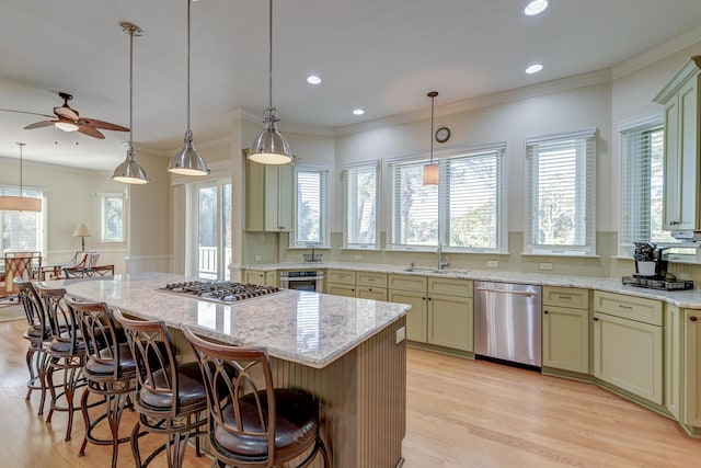 kitchen with a sink, appliances with stainless steel finishes, ornamental molding, a center island, and a kitchen bar