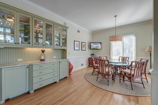 dining room featuring light wood-style floors, a wainscoted wall, visible vents, and crown molding