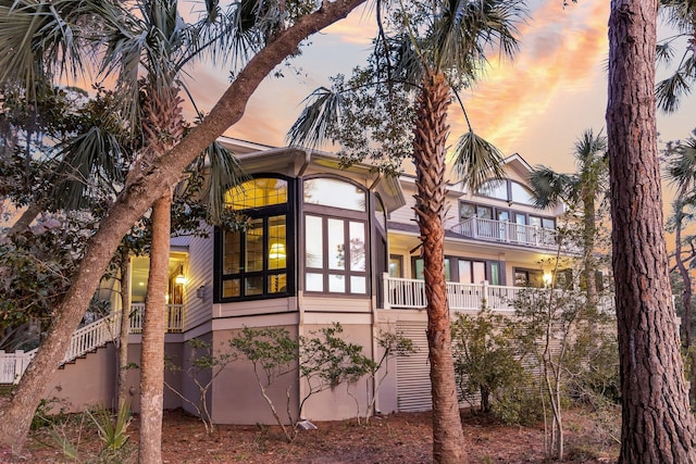 property exterior at dusk with a balcony, stairway, and stucco siding