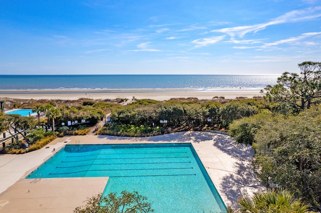 community pool with a patio area, a water view, and a view of the beach