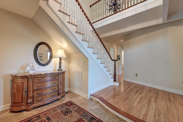 stairway with visible vents, a towering ceiling, baseboards, and wood finished floors