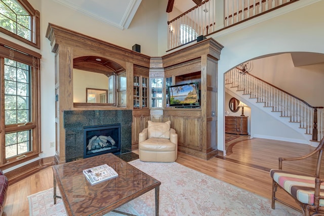 living area featuring stairs, ornamental molding, a tiled fireplace, and wood finished floors