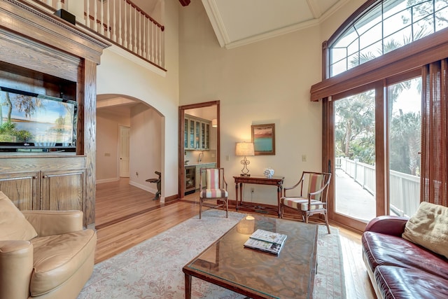 living room featuring arched walkways, ornamental molding, wood finished floors, beverage cooler, and baseboards