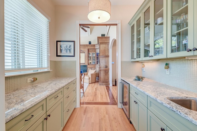 kitchen with arched walkways, light stone counters, backsplash, light wood finished floors, and glass insert cabinets