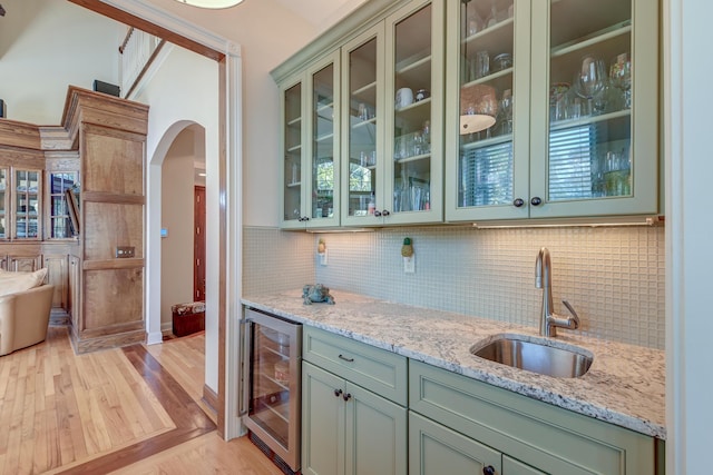 bar featuring arched walkways, beverage cooler, a sink, decorative backsplash, and light wood finished floors