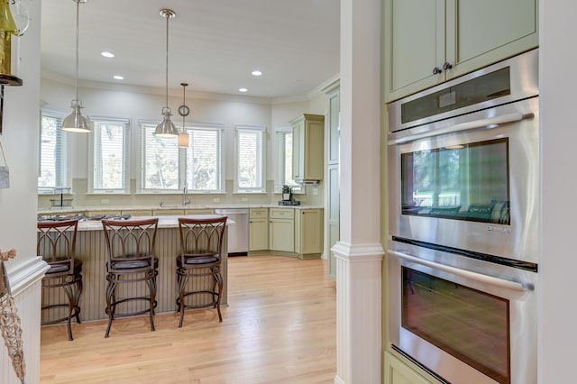 kitchen featuring stainless steel appliances, light countertops, light wood-style flooring, ornamental molding, and a kitchen bar