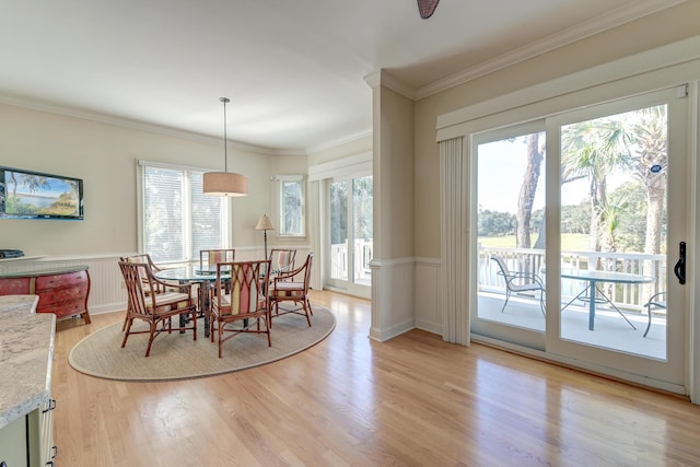 dining area with a healthy amount of sunlight, light wood-style flooring, crown molding, and wainscoting