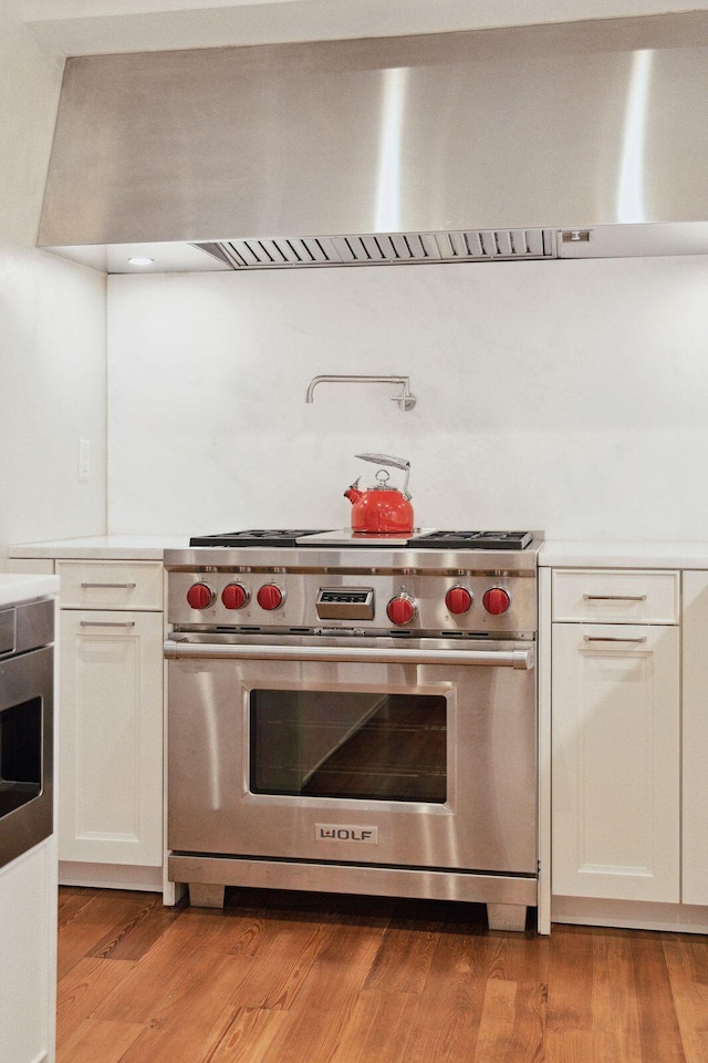 kitchen with white cabinetry, premium range, light hardwood / wood-style flooring, and wall chimney exhaust hood