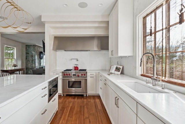 kitchen with white cabinetry, stainless steel appliances, sink, and wall chimney range hood