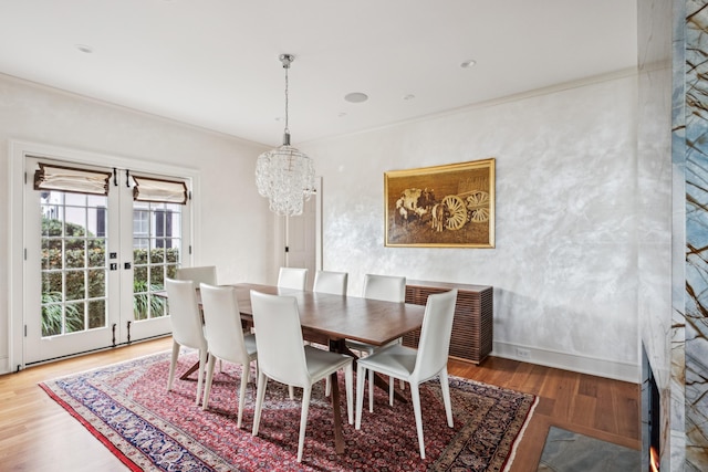 dining space featuring wood-type flooring, ornamental molding, a chandelier, and french doors