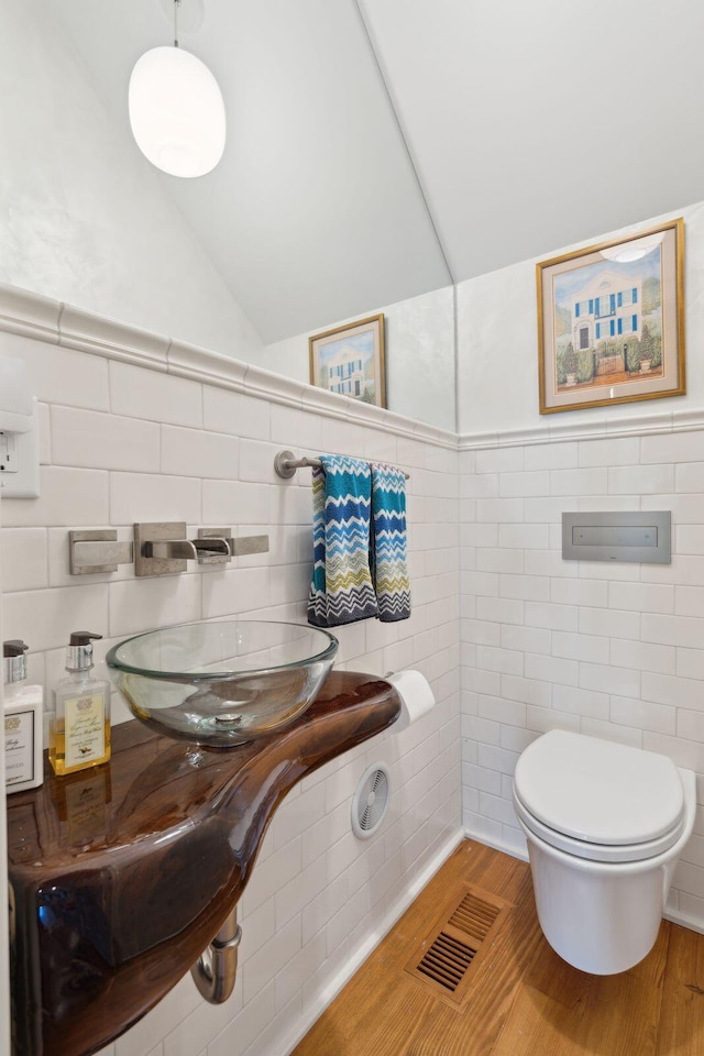 bathroom with wood-type flooring, vaulted ceiling, tile walls, and toilet