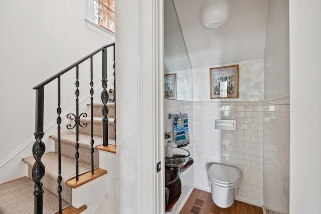 bathroom with wood-type flooring, toilet, and tile walls